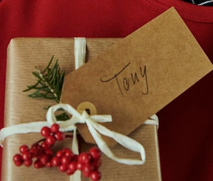 Kleines verpacktes Geschenk mit dem Namensschild 'Tony'. Das Geschenk liegt auf Pyjamas von Calida.