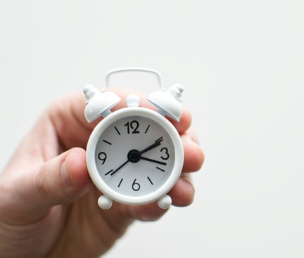 Eine Hand hält einen kleinen weißen Wecker, der 3:10 anzeigt – Symbol für die Schlafenszeit.