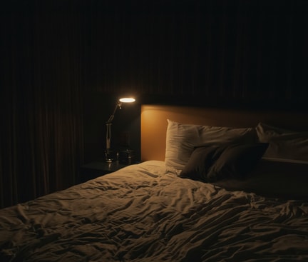 Dunkles Schlafzimmer mit schwacher Beleuchtung durch eine Nachttischlampe, unordentliches Bett – symbolisiert die beklemmende Atmosphäre eines Albtraums.