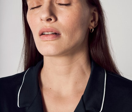 Portrait d'une femme aux yeux fermés et à l'expression neutre, présentant des ridules et des changements cutanés – signes typiques pouvant apparaître pendant la ménopause en raison des fluctuations hormonales.
