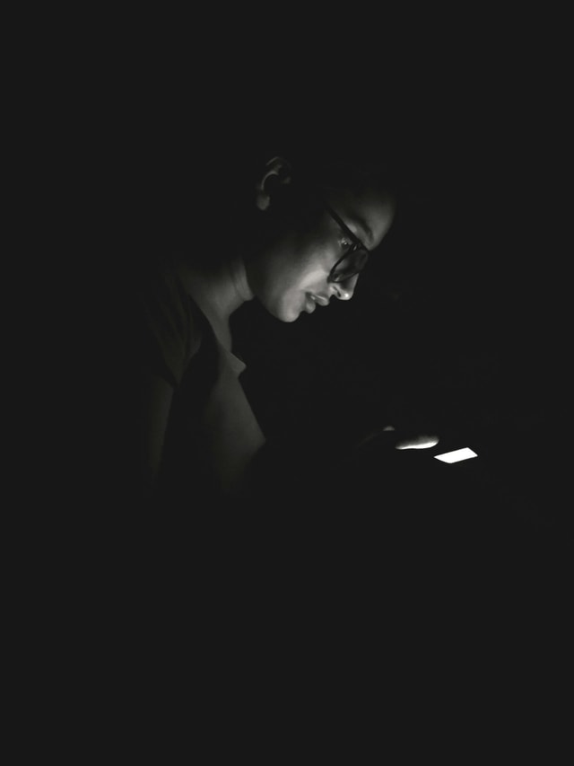 Bild von einer Person im Dunklen, die am Handy ist.