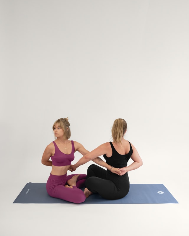 Zwei Frauen in der Yoga-Pose "Drehsitz zu zweit (Matsyendrasana).