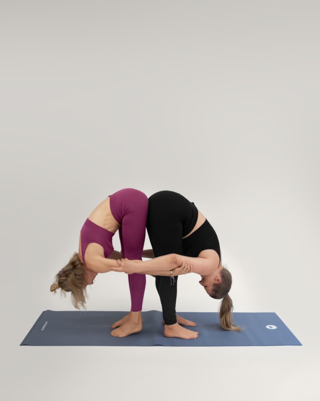 Zwei Frauen in der Yoga-Pose 'Die gemeinsame Vorbeuge' (Uttanasana).