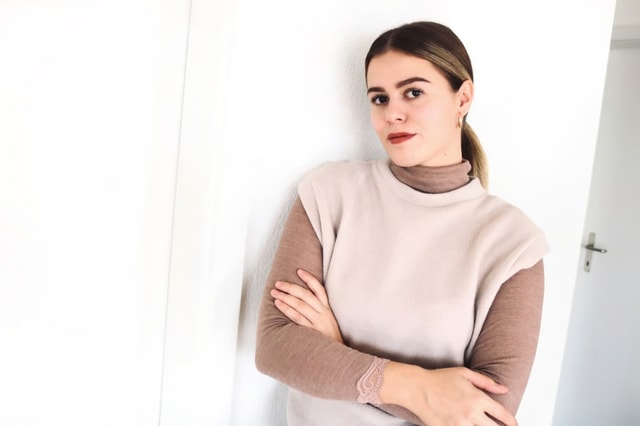 Frau trägt einen braunen Rollkragenpulli unter einem beigen ärmellosen Sweater.