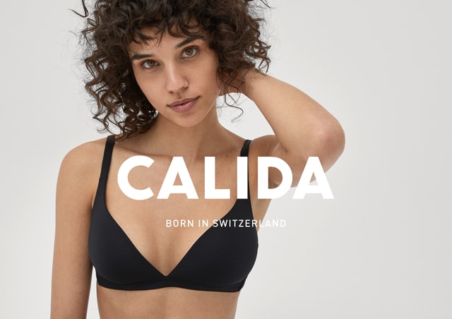 Eine Frau sitzt auf einem weissen Boden und trägt einen schwarzen Triangel-BH und ein schwarzer Panty der Serie ECO SENSE von CALIDA.