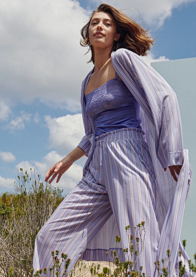 Frau auf einer Wiese trägt violette Kleidung von CALIDA. Spaghetti-Top aus der Serie 'Sensual Secrets' und Hose und Kimono aus der Serie 'Favourites Rosy'.