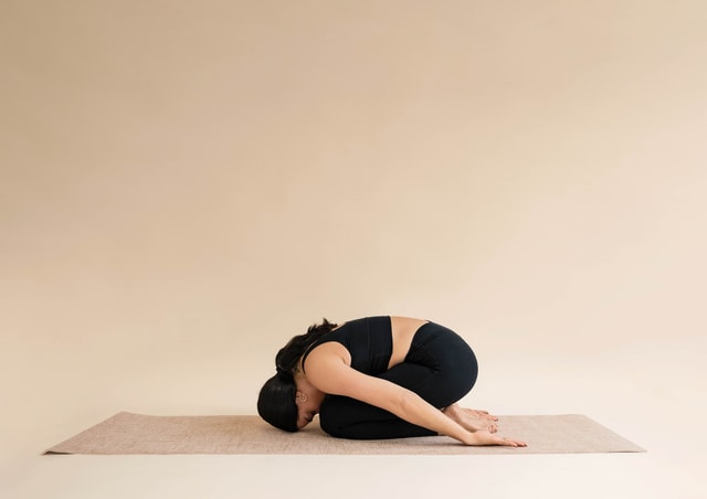 Woman wearing black bustier and black leggings by CALIDA. She does the yoga pose 'The Child'