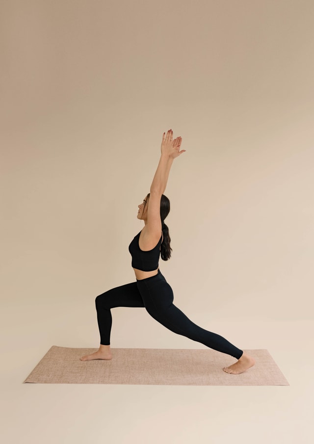 Woman wears black leggings and bustier by CALIDA. She is doing the yoga exercise 'Warrior I'