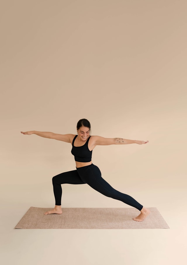 Woman wearing black leggings and black bustier from CALIDA. She does the yoga exercise 'Warrior 2'.