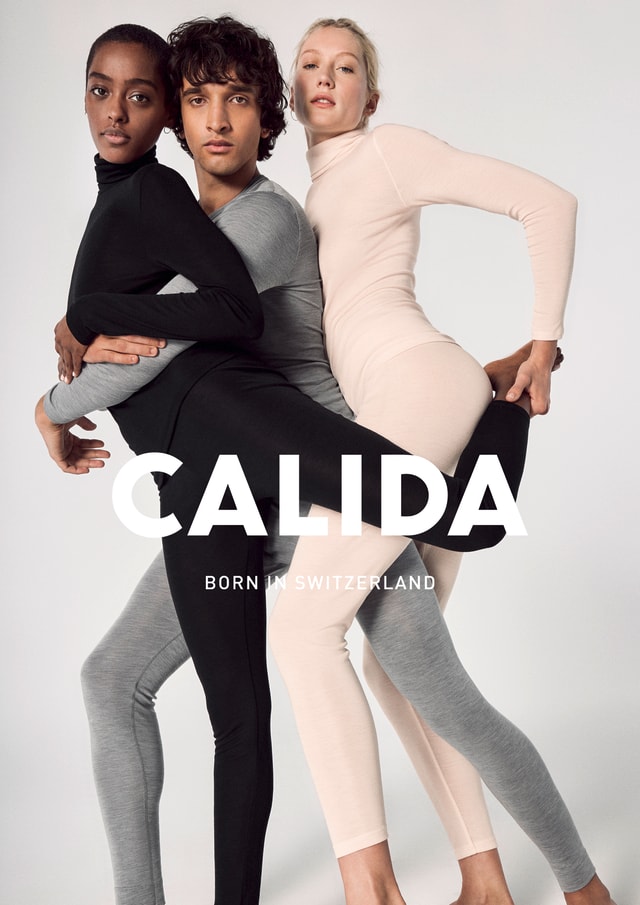 Three models in tight-fitting, long-sleeved Calida outfits in black, grey and beige pose tightly embraced in front of a light background. Lettering ‘CALIDA - Born in Switzerland’.