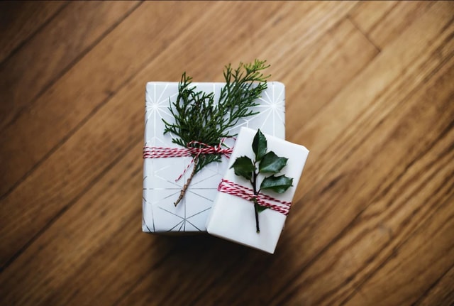 Auf dem Bild sind Geschenke zu sehen, die mit Tannenzweigen verziert sind. Die Tannenzweige sind umwickelt mit einem weihnachtlich roten Geschenkband.