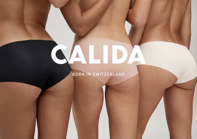 Drei Frauen in nahtloser Unterwäsche in Schwarz, Rosa und Cremeweiß, Rückenansicht. Großes Logo 'CALIDA' mit dem Slogan 'Born in Switzerland' im Vordergrund.