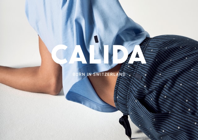 Mann liegt Seitlichen auf einem weißen Boden. Er trägt blaue Nachtwäsche. Großes CALIDA Logo mit dem Slogan 'Born in Switzerland'.