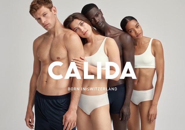 Vier diverse Models in minimalistischer Unterwäsche posieren eng aneinander, mit sanften Gesichtsausdrücken. Im Vordergrund steht der Markenname "CALIDA" mit dem Slogan "BORN IN SWITZERLAND". Das Bild vermittelt ein Gefühl von Nähe, Komfort und Natürlichkeit.