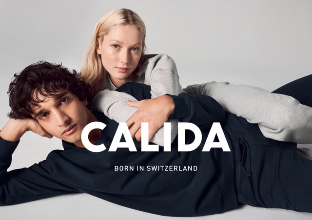 A man and a woman wearing CALIDA nightwear. The CALIDA logo and the slogan ‘Born in Switzerland’ can be seen.
