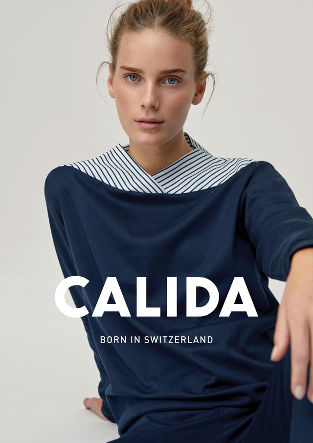 Donna con una maglia blu navy CALIDA con colletto a righe, che guarda la fotocamera; immagine pubblicitaria con la scritta 'CALIDA – Born in Switzerland'.