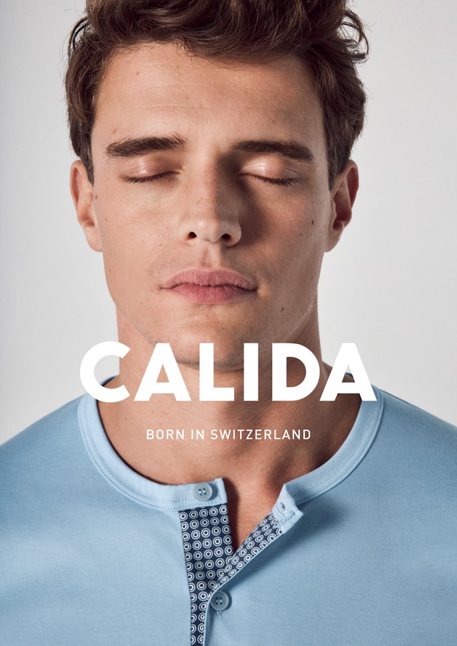 Nahaufnahme eines jungen Mannes mit geschlossenen Augen in einem hellblauen Shirt mit gemustertem Kragen. Text 'CALIDA – Born in Switzerland' über dem Bild.